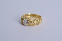 Gold ring with intricate design and a central diamond on a light gray background
