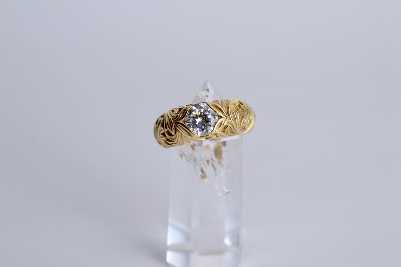 Gold ring with a diamond on a clear stand against a light gray background