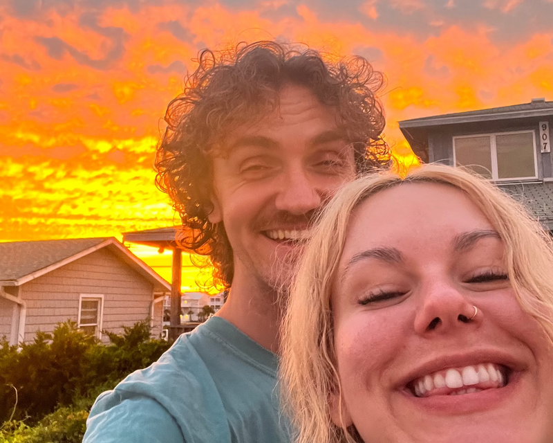 Two people taking a selfie with a vibrant sunset in the background.