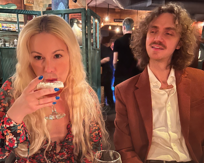 Two people sitting at a table in a restaurant, one holding a glass of wine.