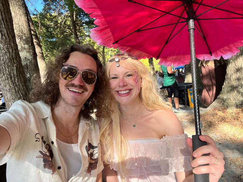 Two people taking a selfie under a red umbrella in a park.