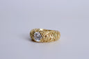 Gold ring with intricate design and a diamond on a light gray background