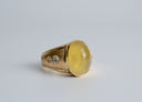 Gold ring with a large yellow gemstone and smaller diamonds on a light gray background
