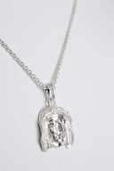 Silver pendant with a face design on a chain against a white background