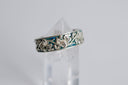 Silver ring with intricate design on a clear stand against a light gray background