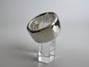 Silver ring on a clear stand against a gray background