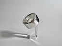 Silver ring with a geometric design on a clear stand against a light gray background