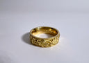 Gold ring with intricate designs on a light gray background