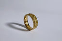 Gold ring with intricate design on a light gray background