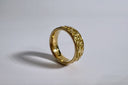Gold ring with intricate design on a light gray background