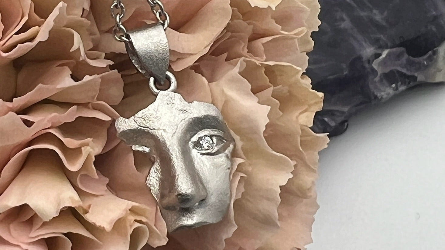 Silver face pendant necklace on a pink carnation flower