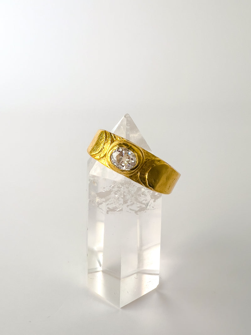 A gold-colored engagement ring with a clear, ornate centerpiece, displayed on a clear crystal stand.