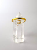 A narrow gold band ring with a minimalist design, featuring a clear crystal on top.