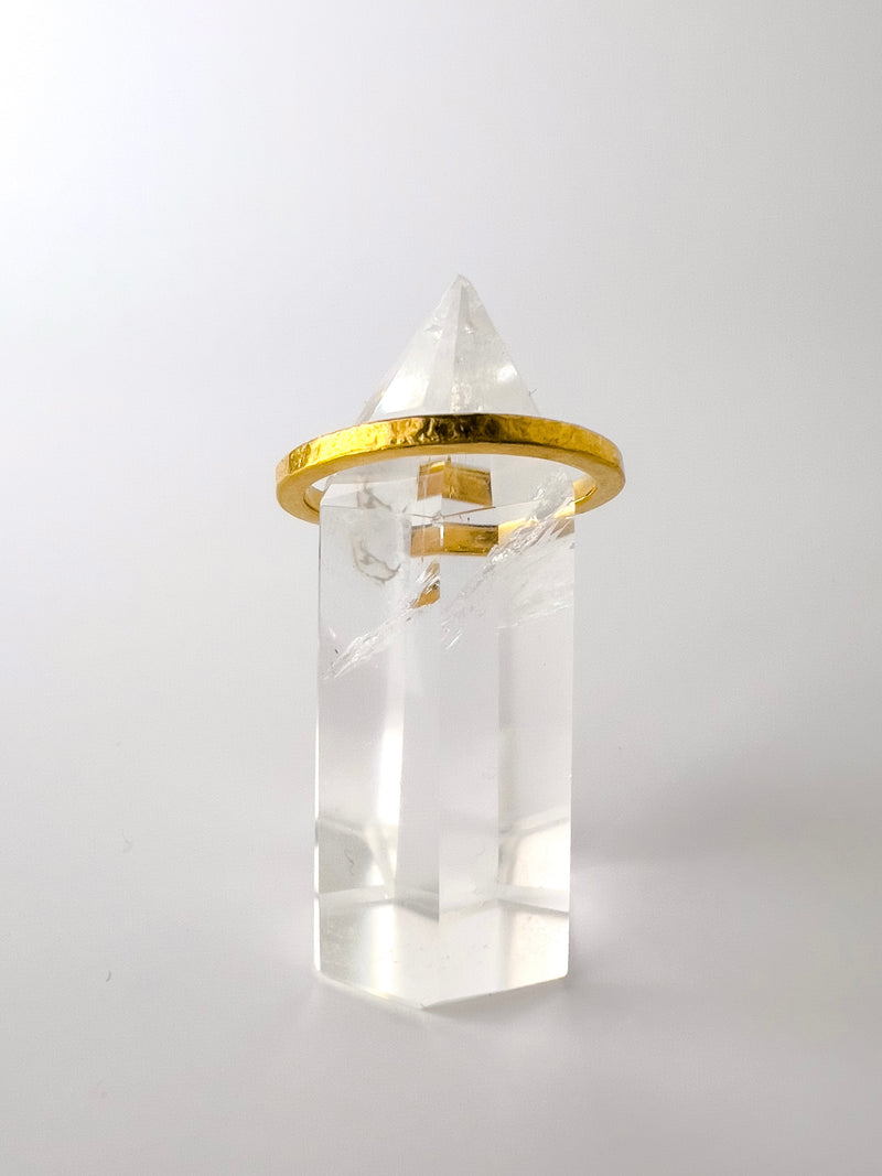 A narrow gold band ring with a minimalist design, featuring a clear crystal on top.