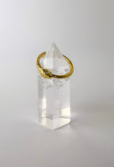 A gold-colored band ring with diamond eyes set in a clear, intricately cut crystal.