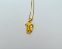 Gold necklace with a face-shaped pendant on a light gray background