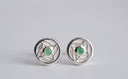 Pair of silver earrings with green gemstones on a light gray background