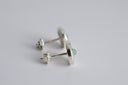 Silver earrings with a green gemstone on a light gray background